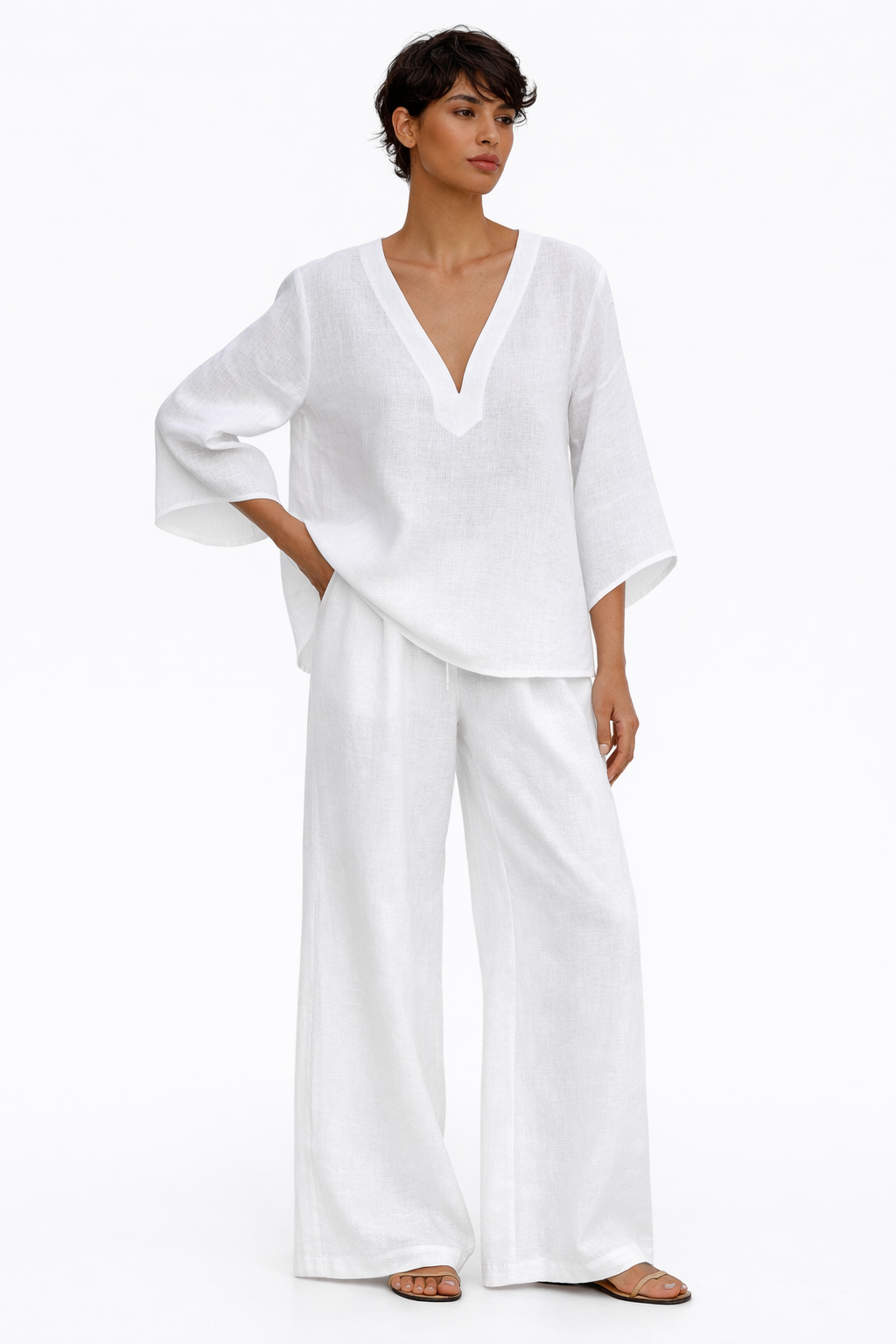 Woman wearing white linen co-ord set with V-neck top and wide-leg drawstring pants, styled against white flower wall.